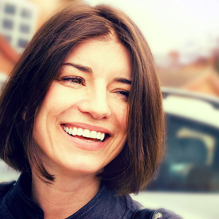 Brunet woman smiling outside of dental office.