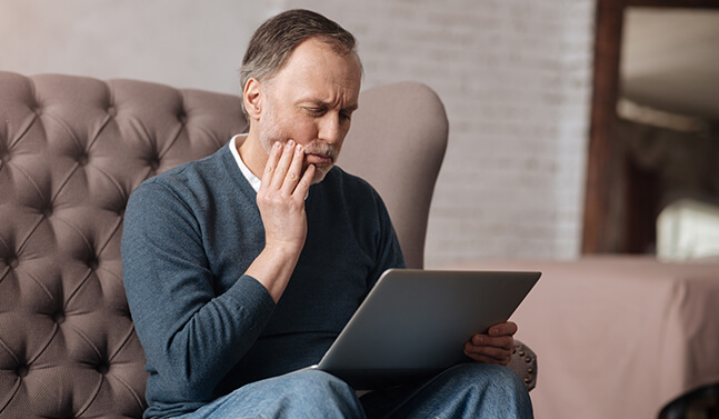 man holding his jaw in pain while looking at his laptop