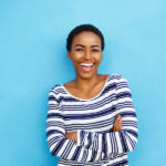 Black woman in a striped shirt against a blue background smiles after professional teeth whitening