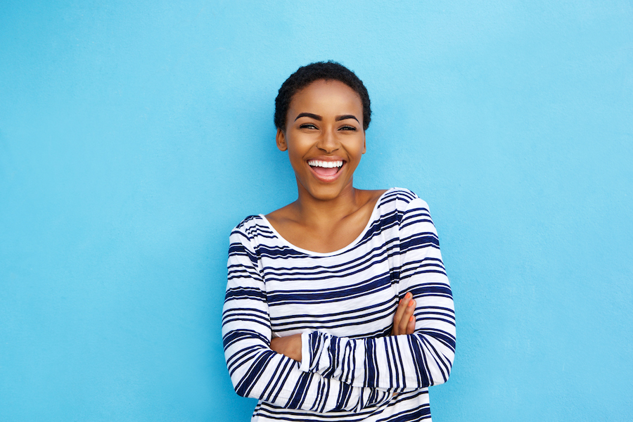 Black woman in a striped shirt against a blue background smiles after professional teeth whitening