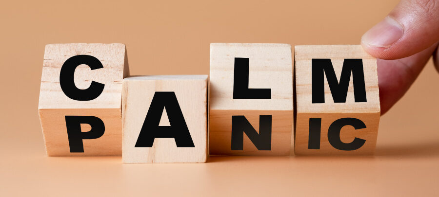 A finger turns wooden blocks from the word PANIC to CALM against a brown background