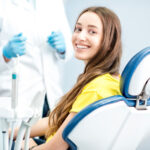 Brunette young woman in a yellow shirt smiles in a dental chair at the dentist