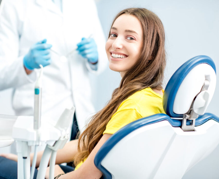Brunette young woman in a yellow shirt smiles in a dental chair at the dentist