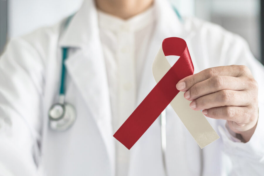 A dentist holds up a cream and red ribbon to indicate oral cancer awareness