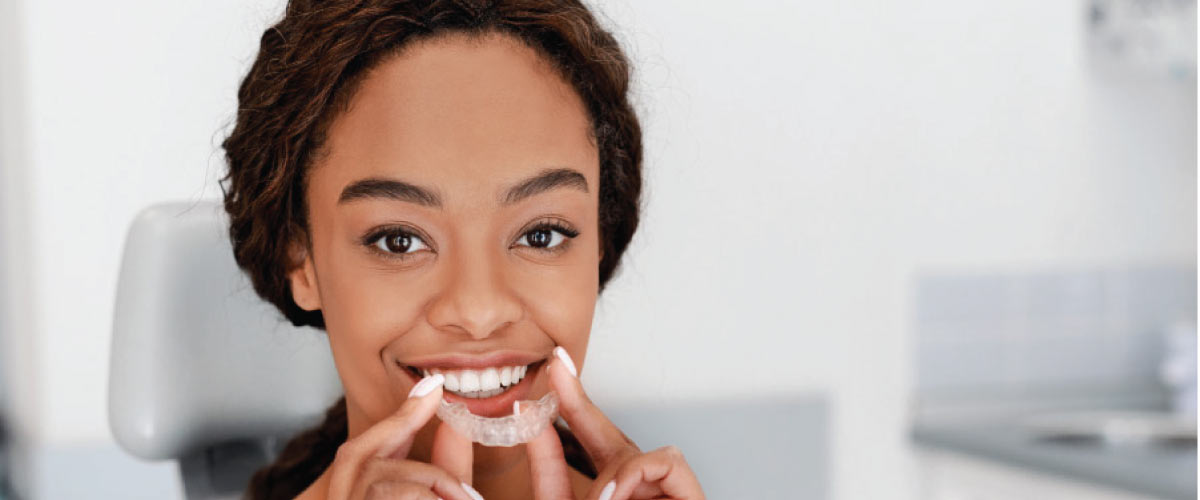 young woman smiles as she inserts her Invisalign clear aligner