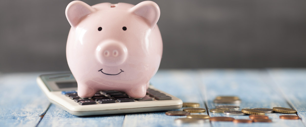 pink piggybank sitting on a calculator next to scattered coins