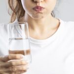 woman with dry mouth drinking water to help symptoms